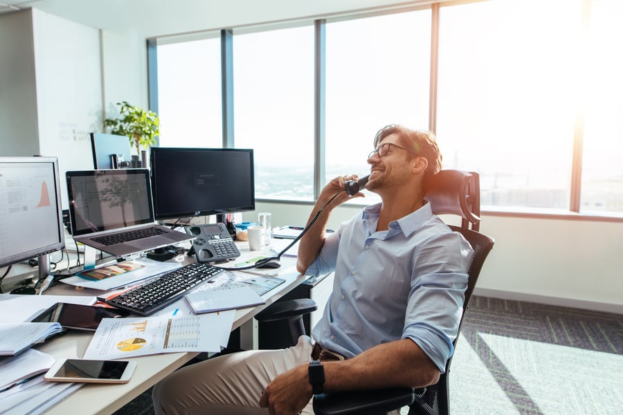Man on a call at a desk with cost dashboards on his screens