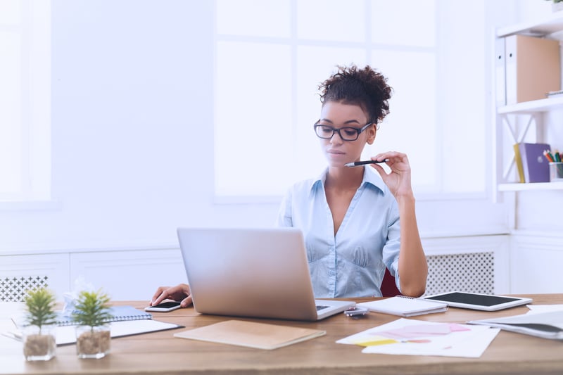 Woman at a desk thinking over figures on her laptop